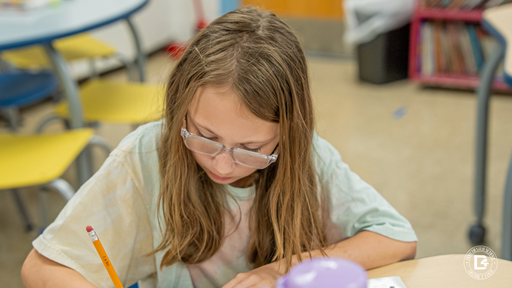 A student wearing glasses concentrates while taking notes about how energy changes form during the hands-on science lesson.