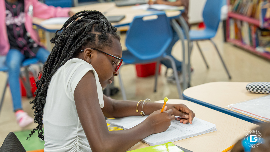 Two students seated at desks look toward the front of the classroom, listening during the interactive lesson.