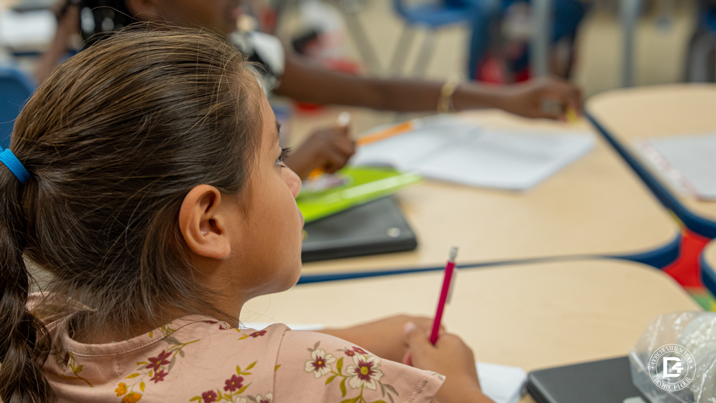 A student with a ponytail listens attentively and holds a pencil during the class discussion.