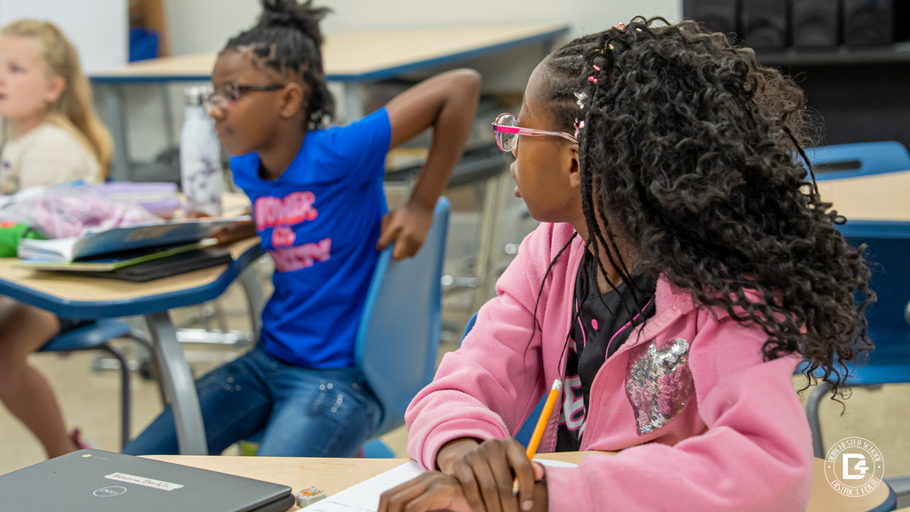 A student with braided hair and glasses writes in her notebook while participating in Mrs. Sawicki’s science lesson.