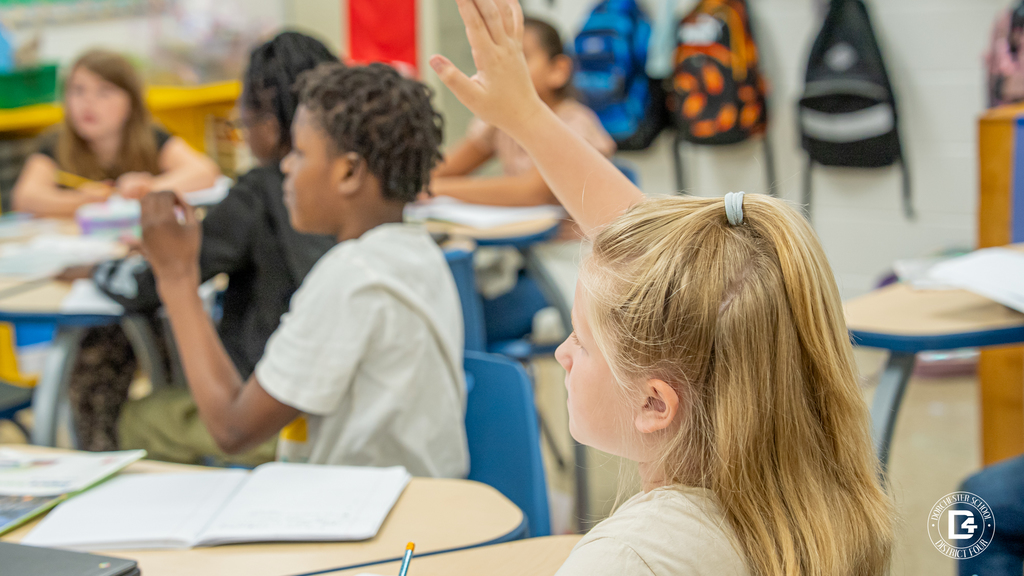 Students sit at round tables as one raises a hand to answer a question during the energy lesson.