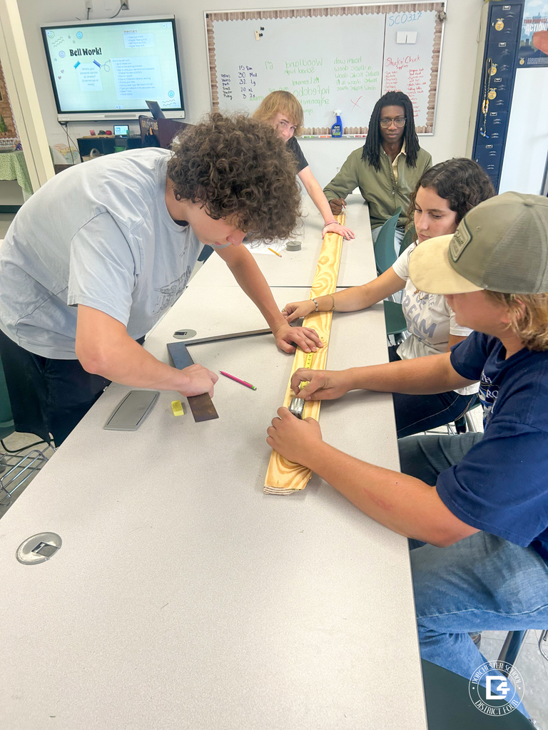 Students in Agricultural Mechanics class work together measuring and marking a wooden board on a classroom table