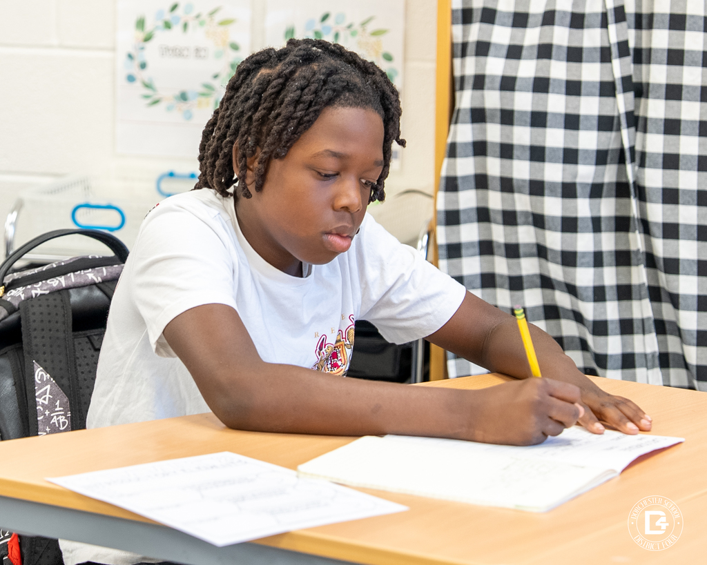 A student focuses intently as he writes in his notebook during a classroom writing activity.