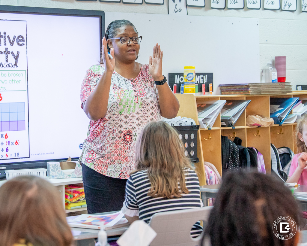 Mrs. Washington uses hand gestures to explain the distributive property of multiplication to her class as students follow along.