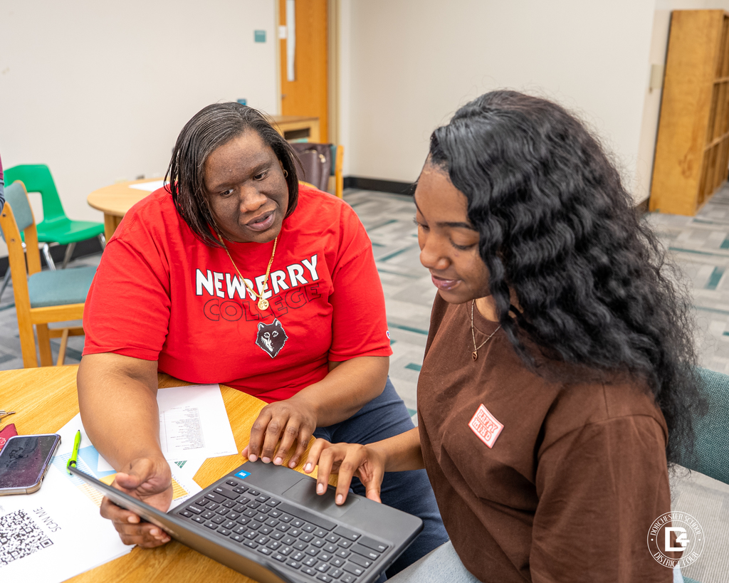 Ms. Thompson, in a red Newberry College shirt sits beside a student and points at a laptop screen as they review application materials together.