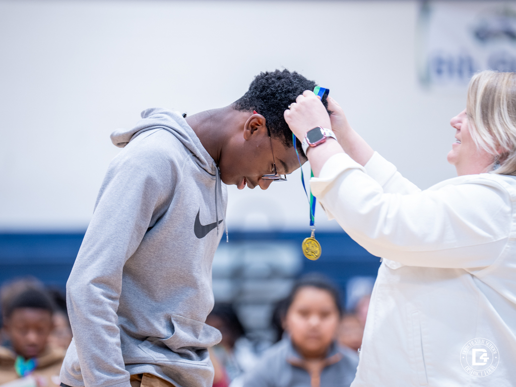 A teacher places a gold medal around a student’s neck during the Woodland Middle School Quarter 1 Awards Day celebration.