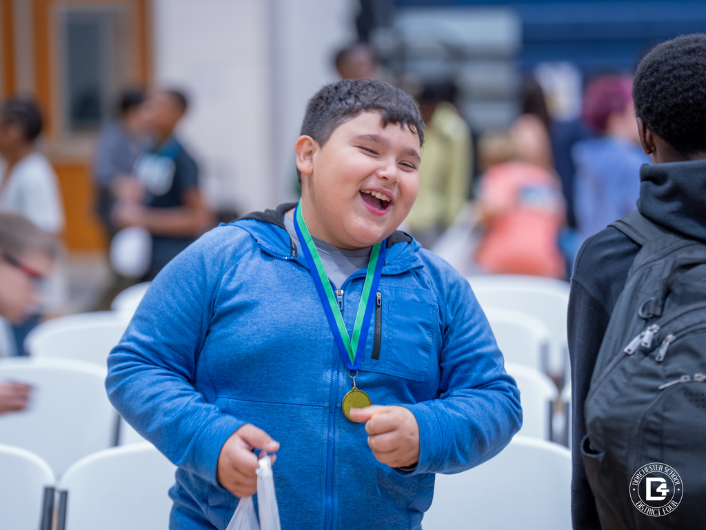 A student wearing a blue hoodie and gold medal smiles proudly after receiving recognition at Woodland Middle School’s Quarter 1 Awards Day.