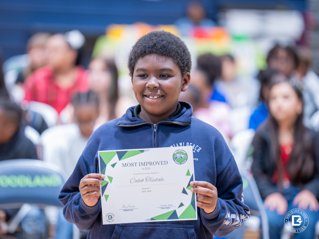 A smiling student holds a “Most Improved” certificate in English Language Arts during Woodland Middle School’s Quarter 1 Awards Day ceremony.