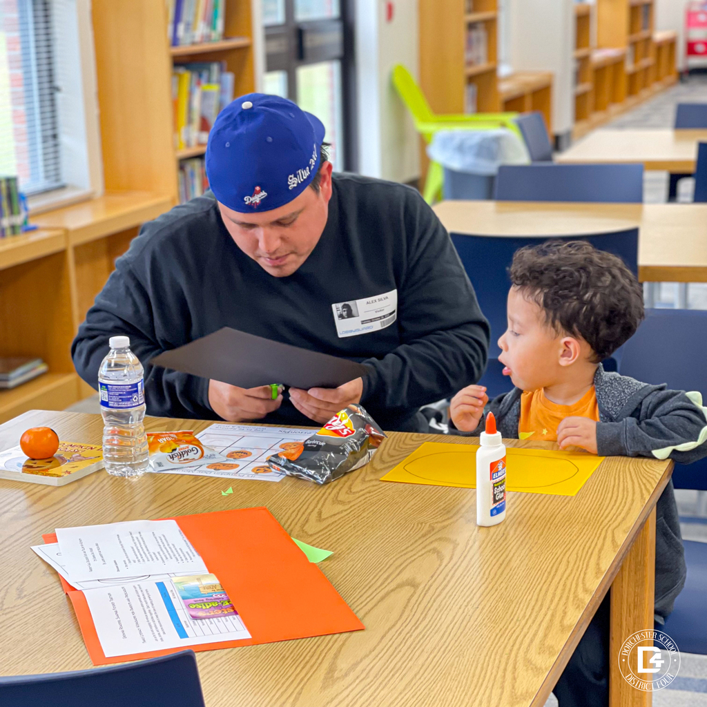 Child focused on cutting black paper for a pumpkin craft while supplies, snacks, and glue sit on the table.