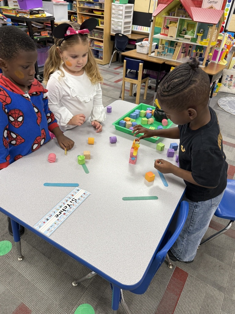 Students in Mrs. Forest’s Pre-Kindergarten class at Williams Memorial Elementary School work together on a Halloween-themed STEM challenge. Each group uses colorful blocks, linking cubes, and craft sticks to build a gate for five little pumpkins after reading Five Little Pumpkins. Children dressed in costumes—princesses, superheroes, and storybook characters—focus intently as they design, test, and adjust their creations, demonstrating teamwork, problem-solving, and persistence.