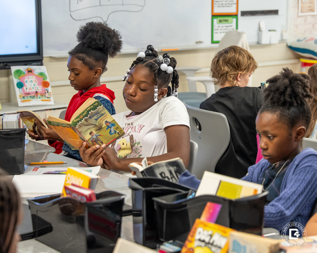 A group of students sit together reading various books, each focused on their story during class reading time.