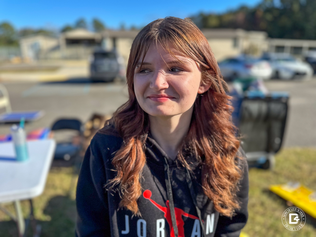 A student with long reddish hair wearing a black Jordan hoodie standing outdoors and looking slightly to the side.