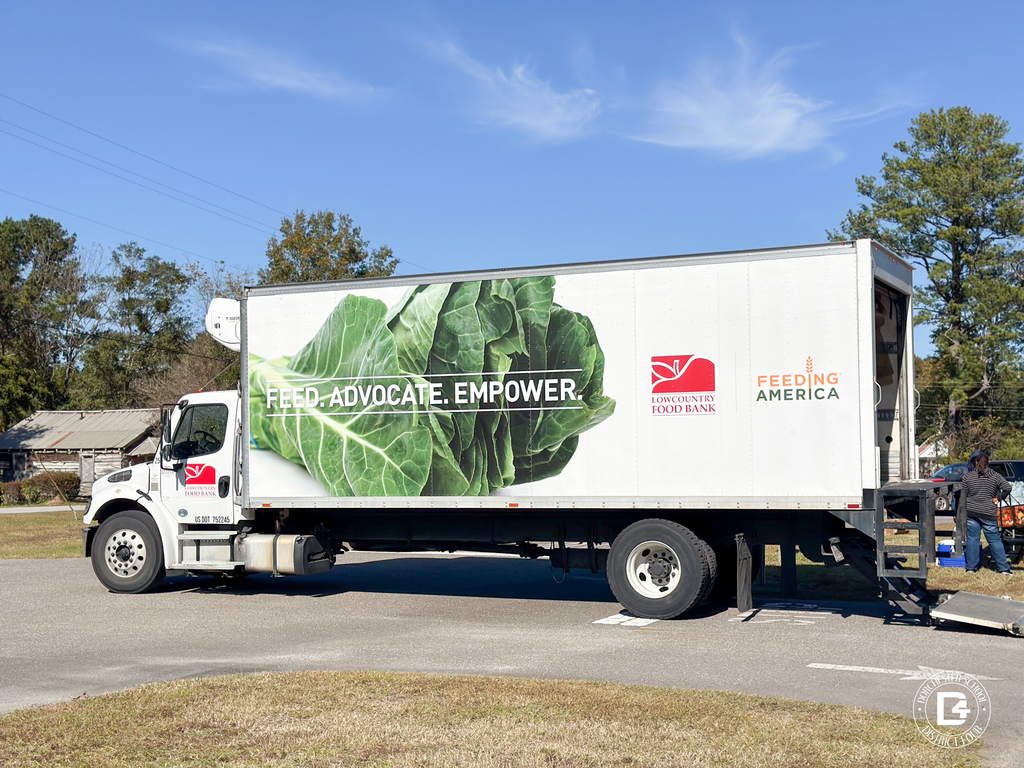 A Lowcountry Food Bank truck parked outdoors with the slogan Feed. Advocate. Empower. displayed alongside large leafy green imagery.