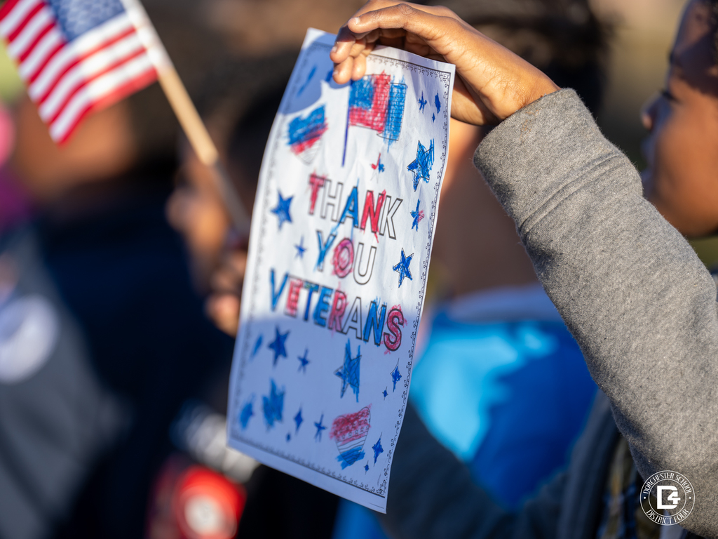 A close-up of a child holding a hand-colored sign that says Thank You Veterans alongside a small American flag.