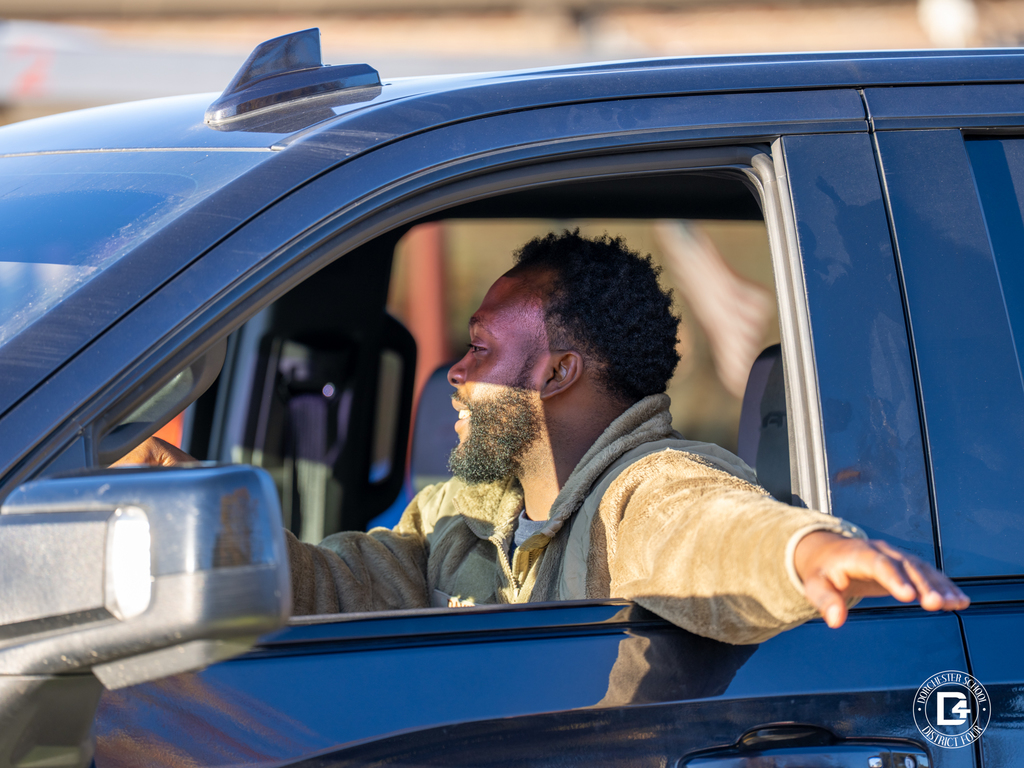 A man in a truck leans out and waves with a smile as he drives through the parade route.