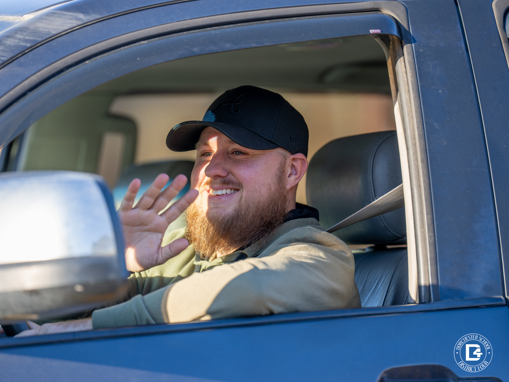 A man in a pickup truck smiles and waves from the driver’s seat during the parade.
