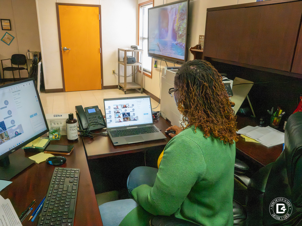 School counselor Tamara Boyd sits at her desk coordinating the virtual career fair, with multiple monitors displaying the online event platform and participant grid.