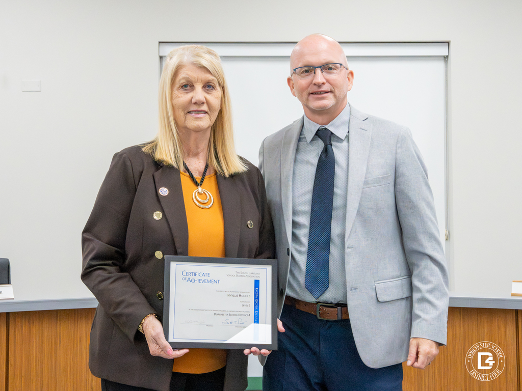 Board member Phyllis Hughes holds a Certificate of Achievement while standing beside Superintendent Jeffrey Beckwith in the DD4 board room.