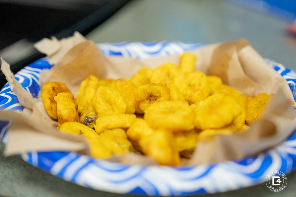 A close-up of a blue paper plate filled with freshly fried golden plantains.