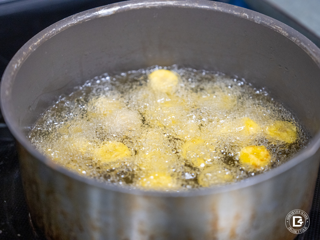 A pot of hot oil on a stovetop as sliced plantains fry and bubble.