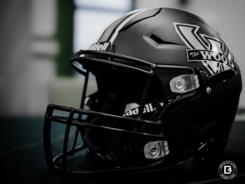 A matte black Woodland football helmet sits on a table, featuring the large W logo and face guard in sharp focus.