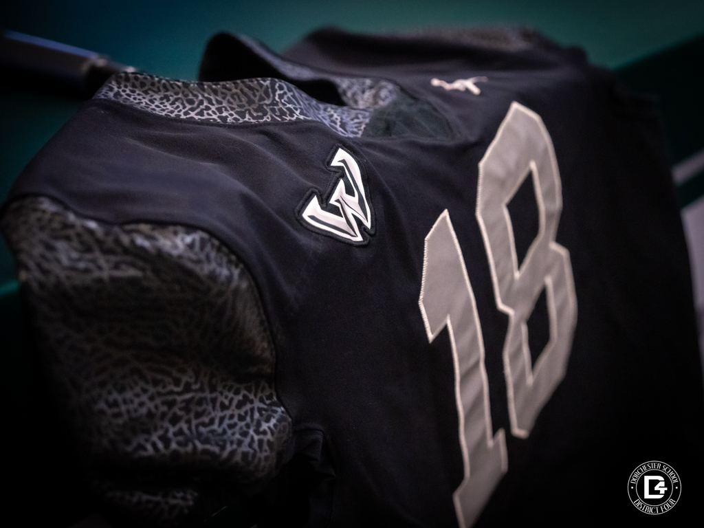 A black Woodland football jersey with the number 18 lies folded on a table, showing the silver W logo and textured shoulder design.
