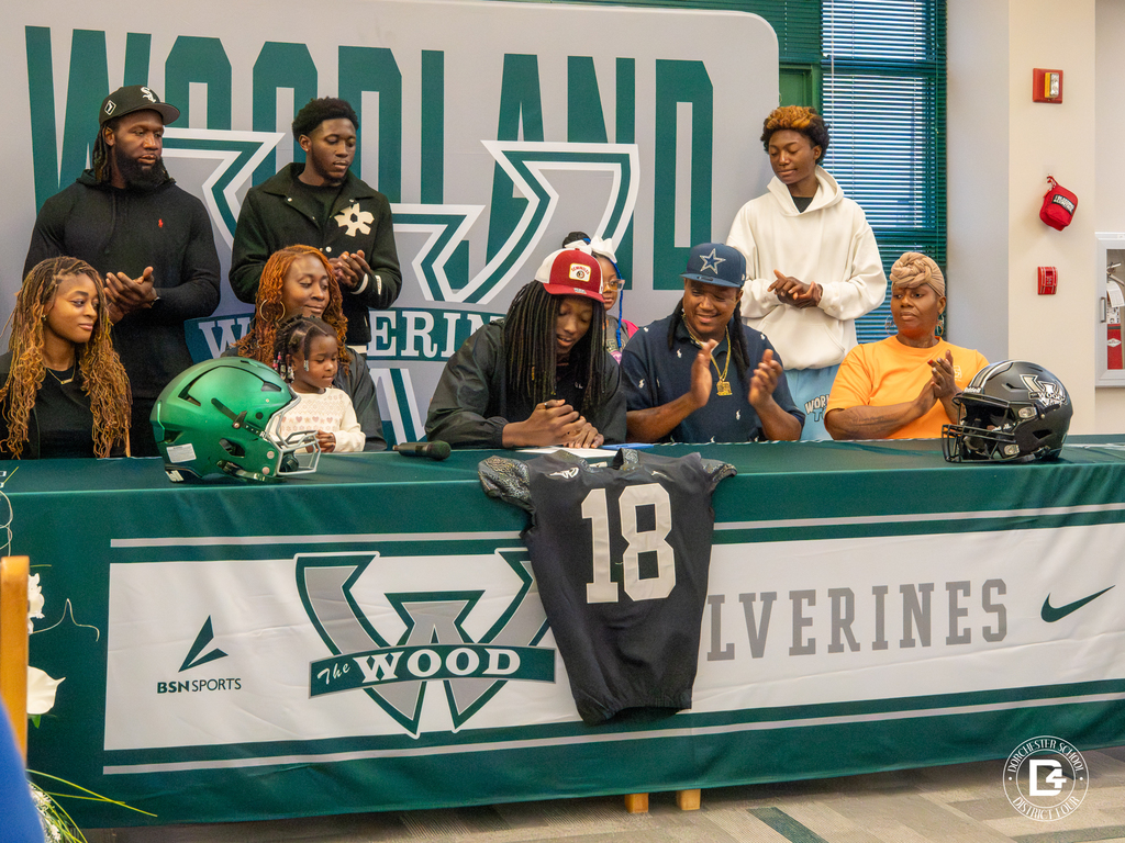 Jaemin Pinckney sits at the table with his family and supporters behind him during the signing ceremony.