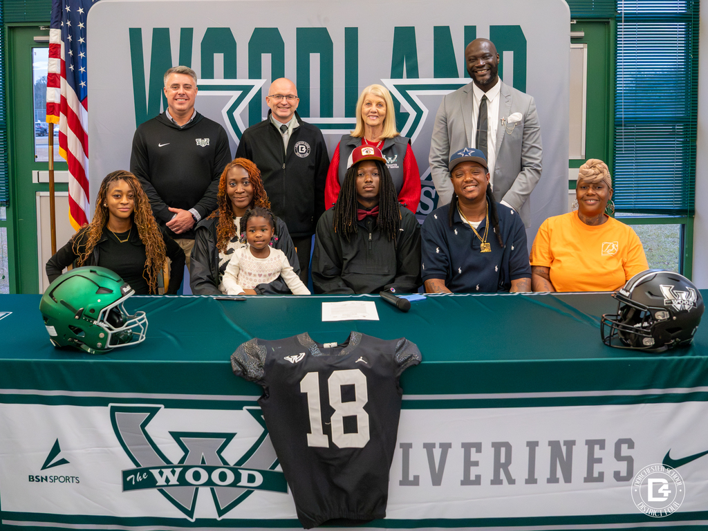 Administrators and school leaders stand behind Jaemin Pinckney and his family at the signing table.