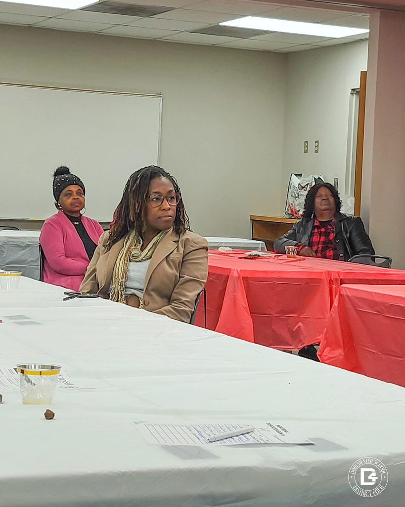 Community members sit at tables listening attentively during a Dorchester School District Four mentoring program meeting, showing engagement and interest in supporting students.