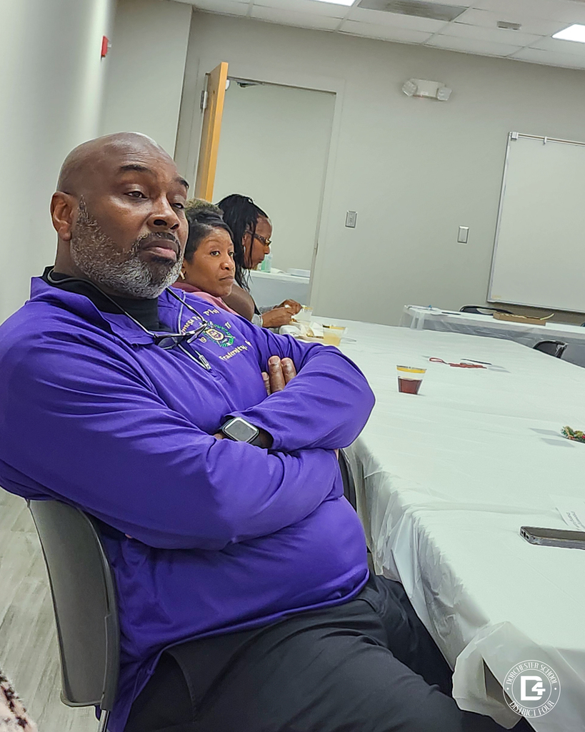 Community mentors sit around a table listening during a Dorchester School District Four mentoring program meeting, reflecting strong community involvement and commitment.