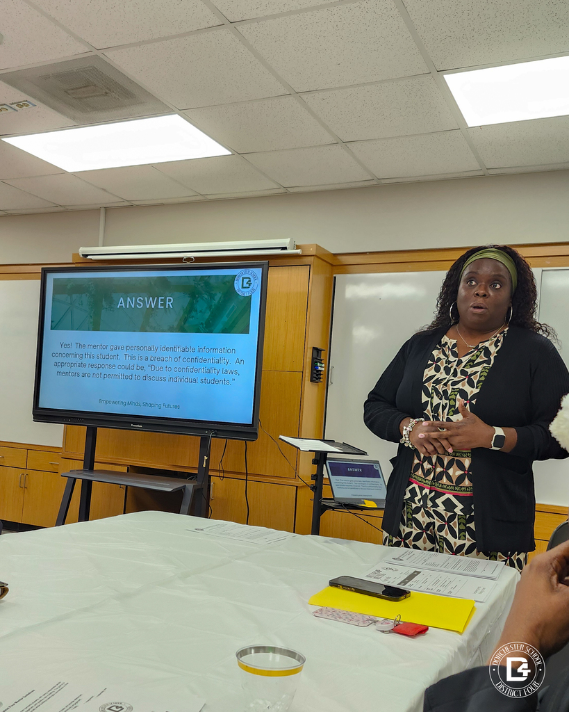 A presenter speaks beside a screen discussing confidentiality and mentor responsibilities during a Dorchester School District Four mentoring program training session.
