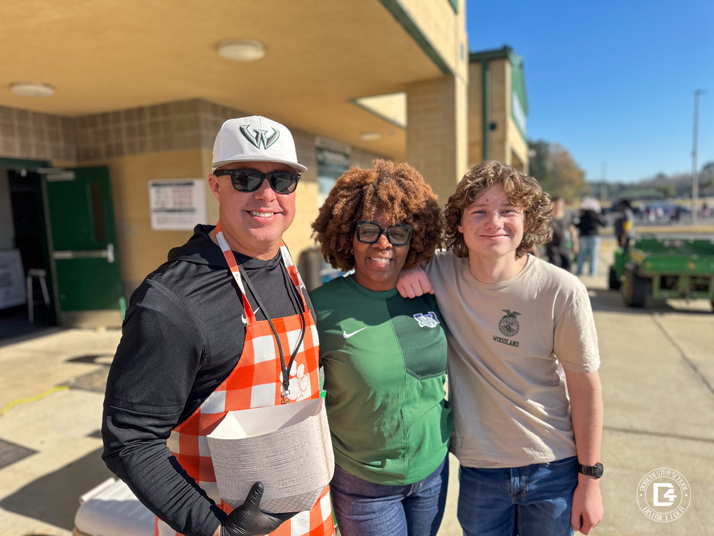 A staff member wearing an apron stands with two others outside Woodland High School, smiling during the Christmas at DD4 event.