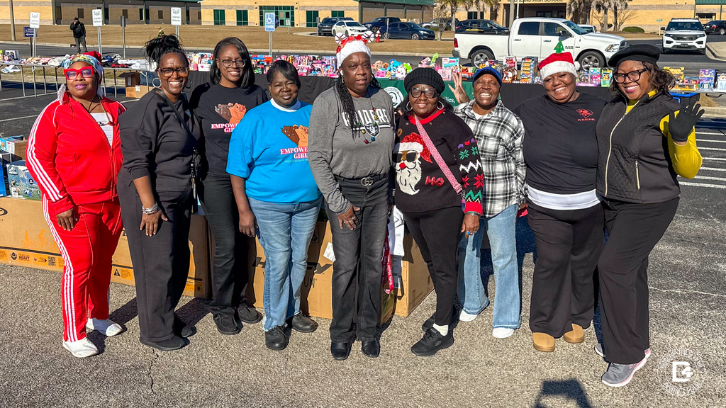A group of community volunteers pose together in front of tables filled with donated toys and gifts at Christmas at DD4.