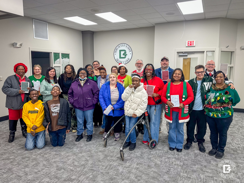 Group photo inside a Dorchester School District Four meeting room showing students and staff from Woodland holding handmade Christmas cards, smiling and standing together in festive holiday attire during a directors meeting.