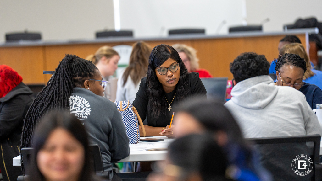 Group of educators seated at a table reviewing materials and working on laptops during professional development.