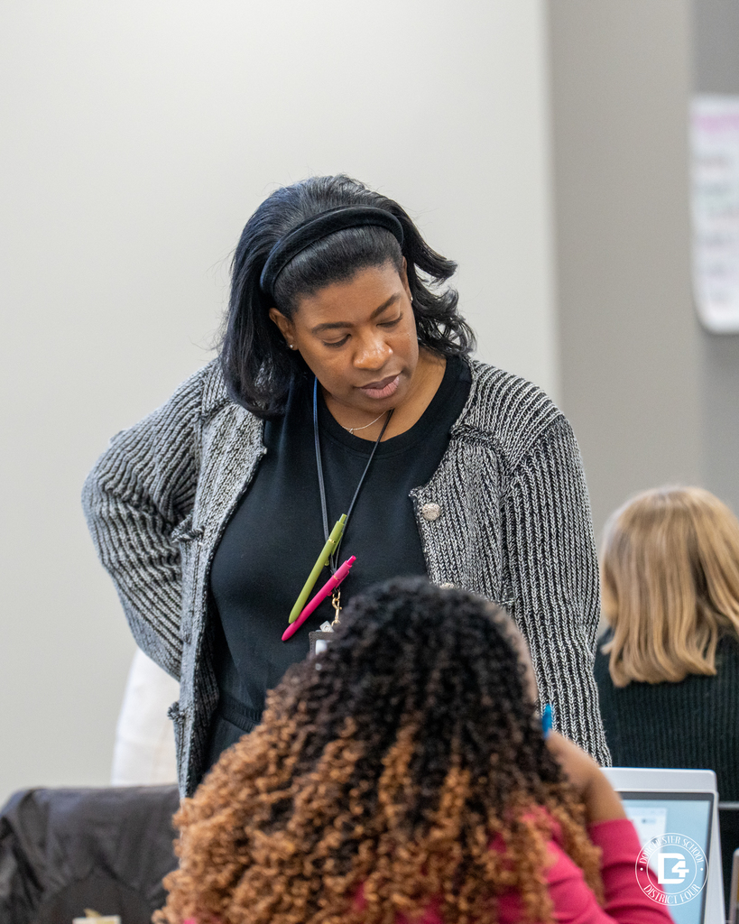 An educator stands beside a table speaking with participants as they work during a professional development session.