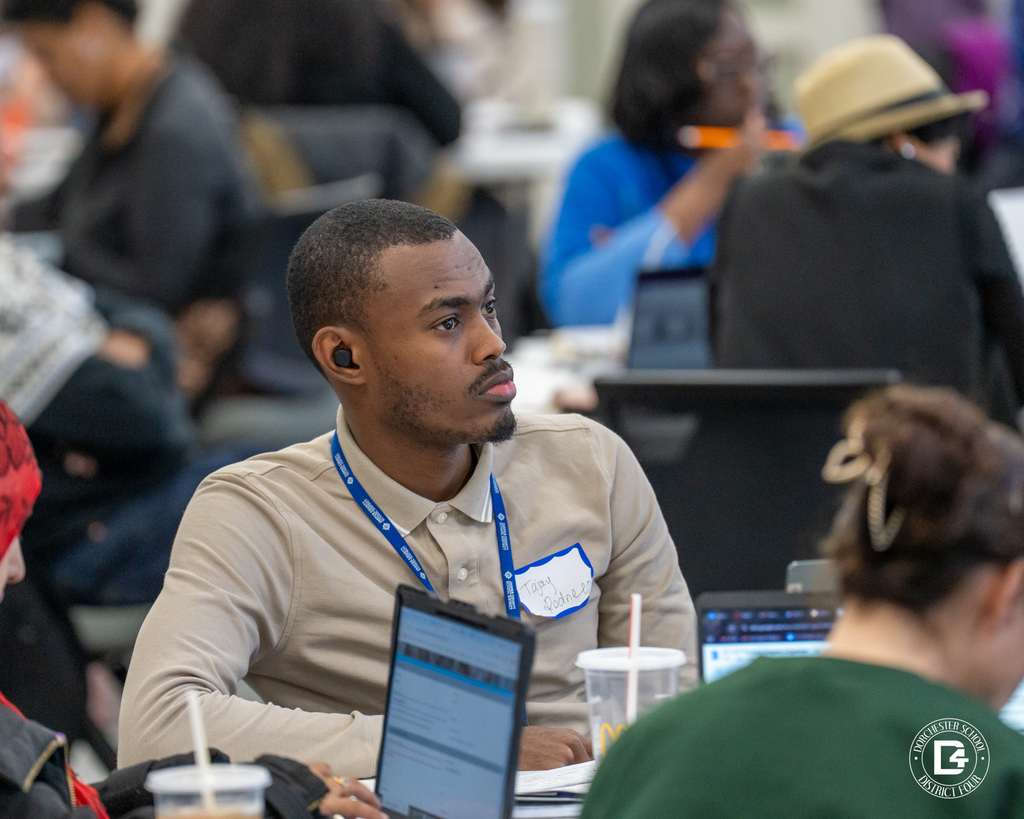 Close-up of an educator wearing a name tag, listening attentively during a group discussion at professional development.
