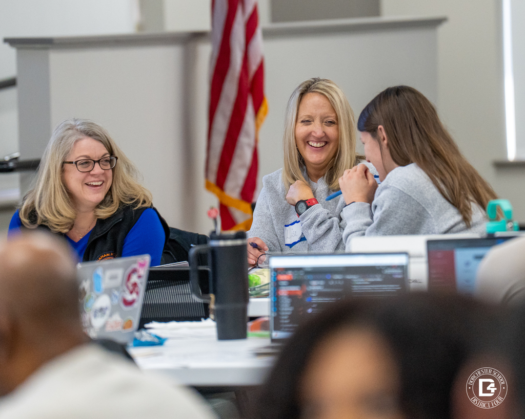 Three educators smiling and talking together at a table during a collaborative professional development activity.