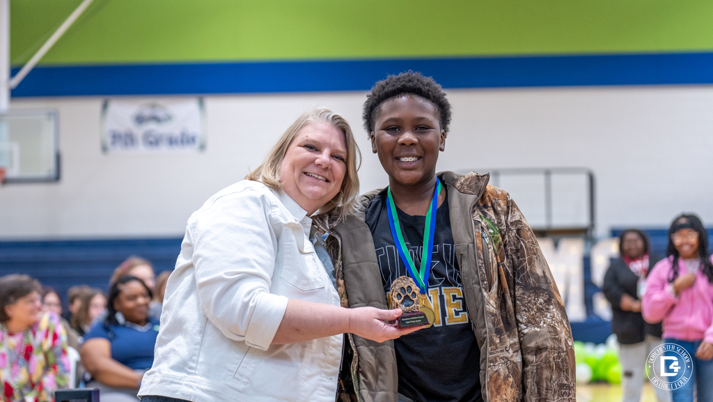 A Woodland Middle School staff member and student smile while holding a wolf-themed academic award during the Quarter 2 awards ceremony.
