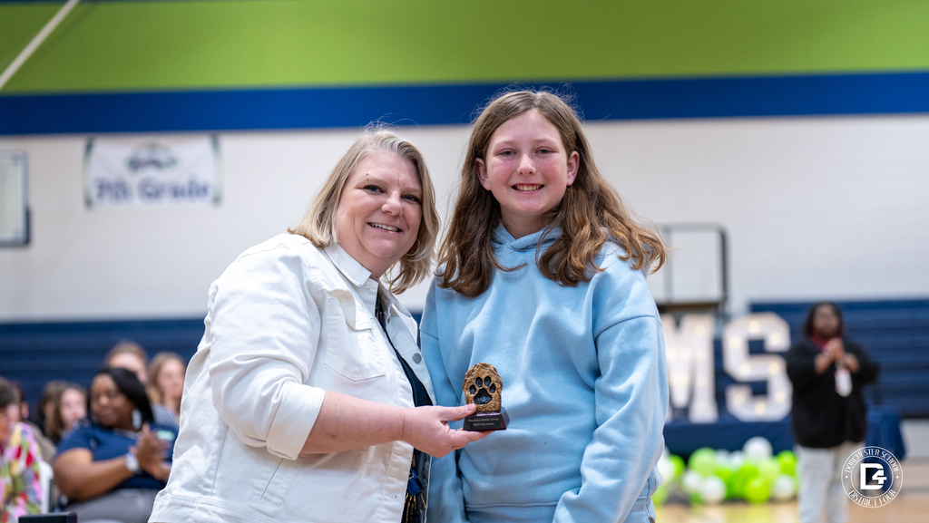 A Woodland Middle School staff member and student pose together holding an academic award during the Quarter 2 awards ceremony.