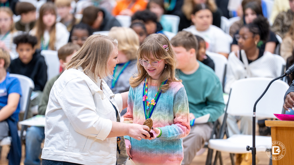A Woodland Middle School staff member and student smile while holding a wolf-themed academic award during the Quarter 2 awards ceremony.