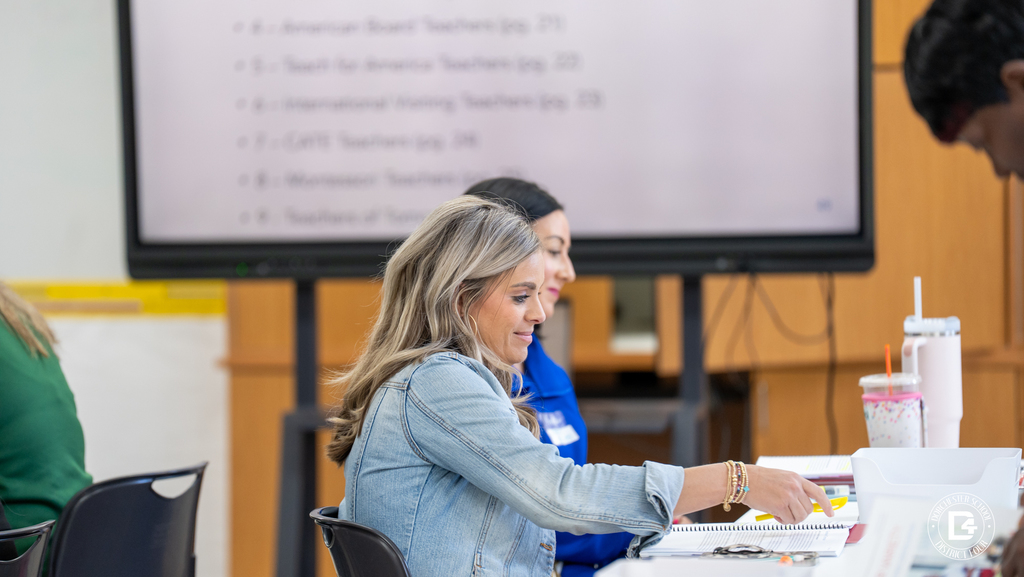 Teachers engage in focused conversation during mentor training, with notebooks, binders, and materials spread across the table.