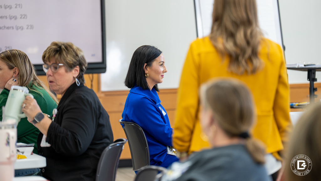 Two educators collaborate during mentor training as a facilitator in a yellow jacket moves between tables to support discussion.