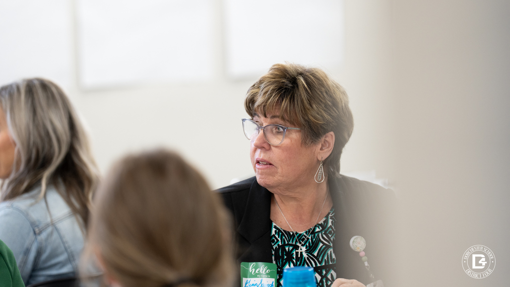 A teacher listens attentively during mentor training while seated among colleagues in a classroom setting.