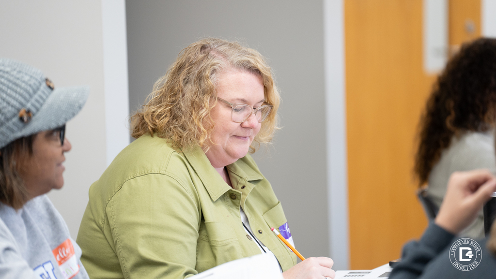 A teacher listens attentively during mentor training while seated among colleagues in a classroom setting.
