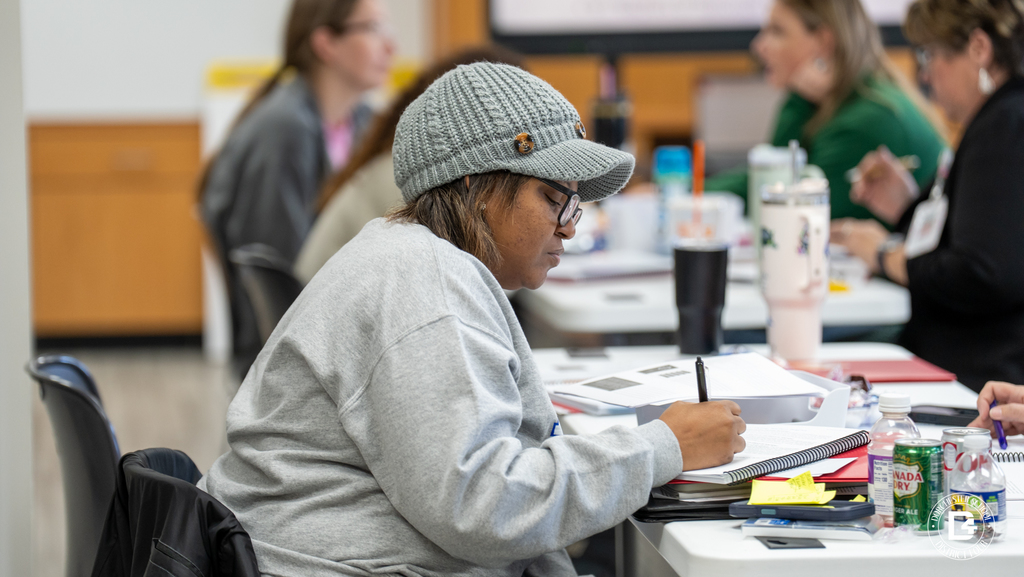 A teacher wearing a knit cap writes notes in a workbook during Dorchester School District Four Teacher Mentor Training.