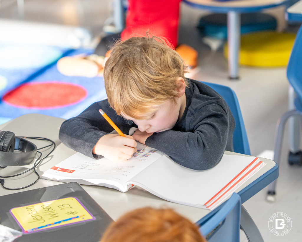 A first-grade student leans over a workbook, writing answers during independent math practice.