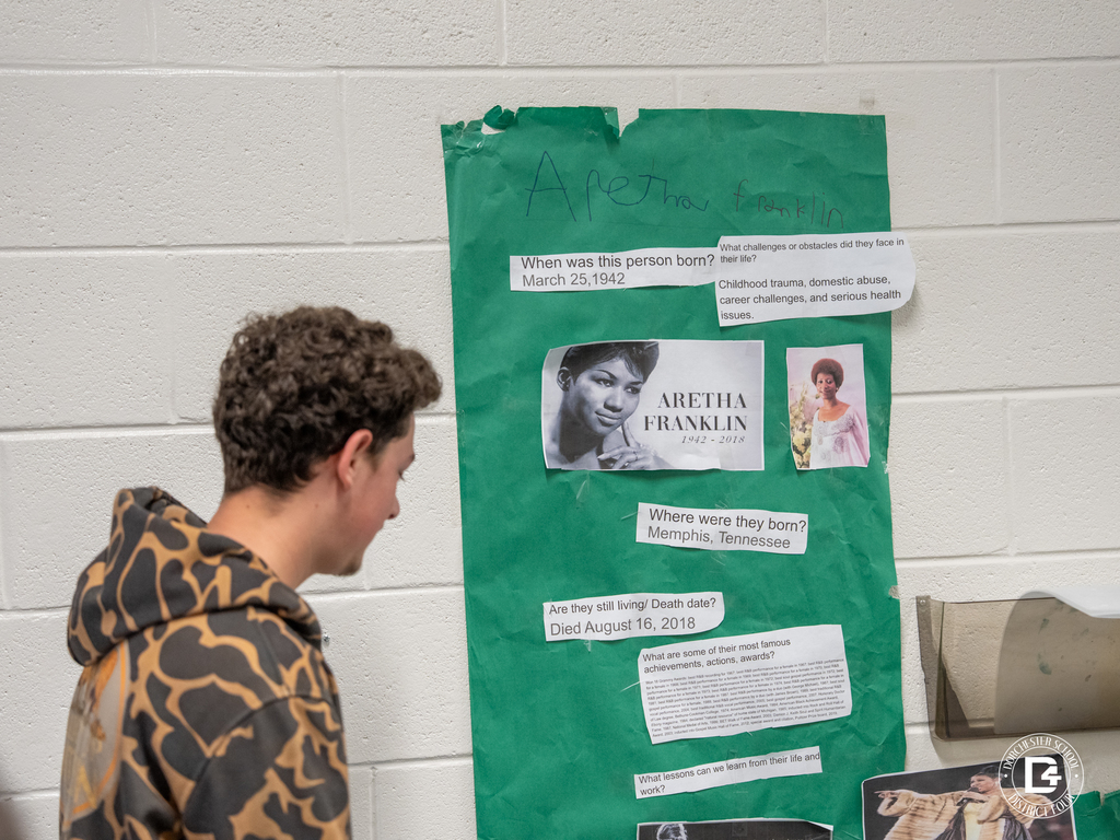 A student studies a green poster about Aretha Franklin, which includes her birth date, achievements, and photos from different stages of her life.