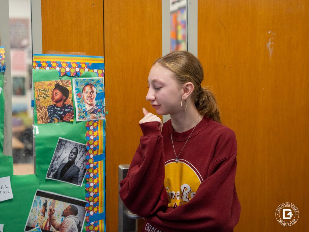 A student stands beside a decorated classroom door featuring artwork and portraits of influential African Americans, looking thoughtfully at the display.