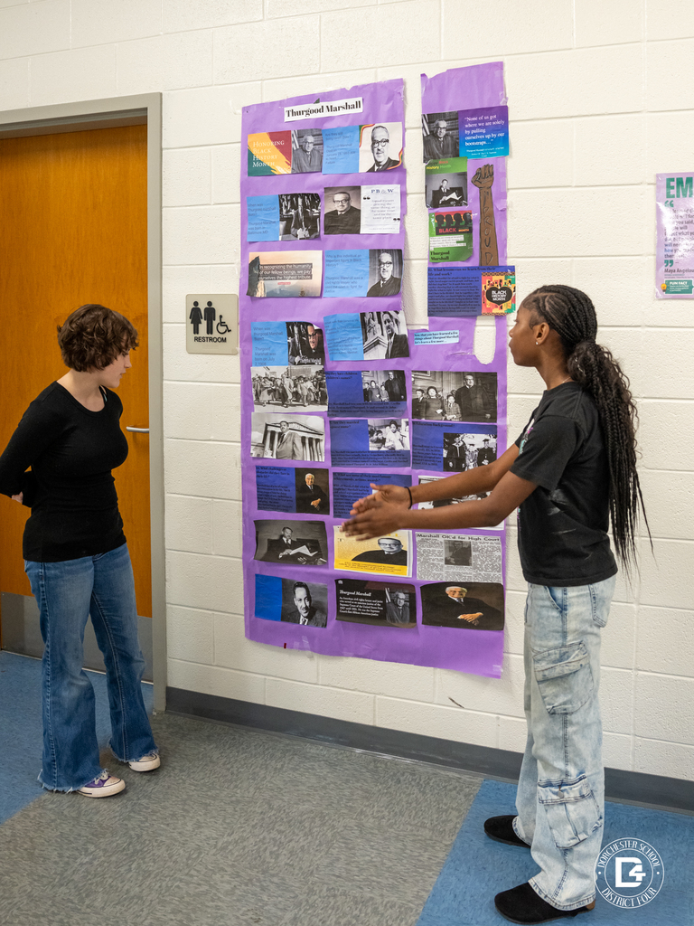 Two students stand in front of a large purple poster about Thurgood Marshall, reviewing images, quotes, and historical information posted on the wall.
